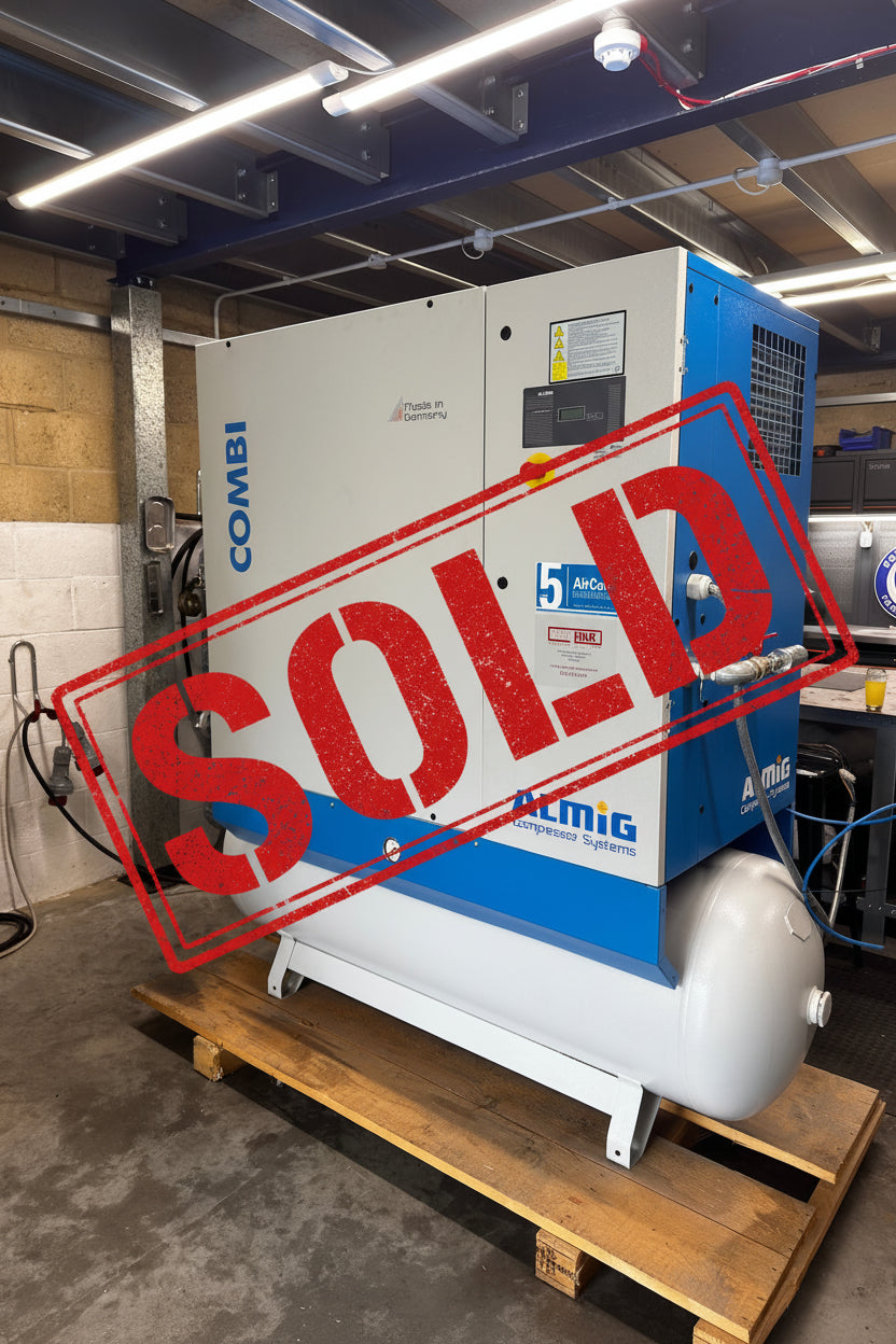 A large industrial air compressor unit with a white and blue cabinet and a white cylindrical tank, sitting on a wooden pallet in a workshop or garage setting. Visible branding includes COMBI on the side and ALMIG on the front panel.