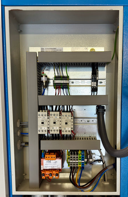 Open industrial electrical control panel showing internal components including contactors, terminal blocks, wiring, and a black flexible conduit inside a metal cabinet.