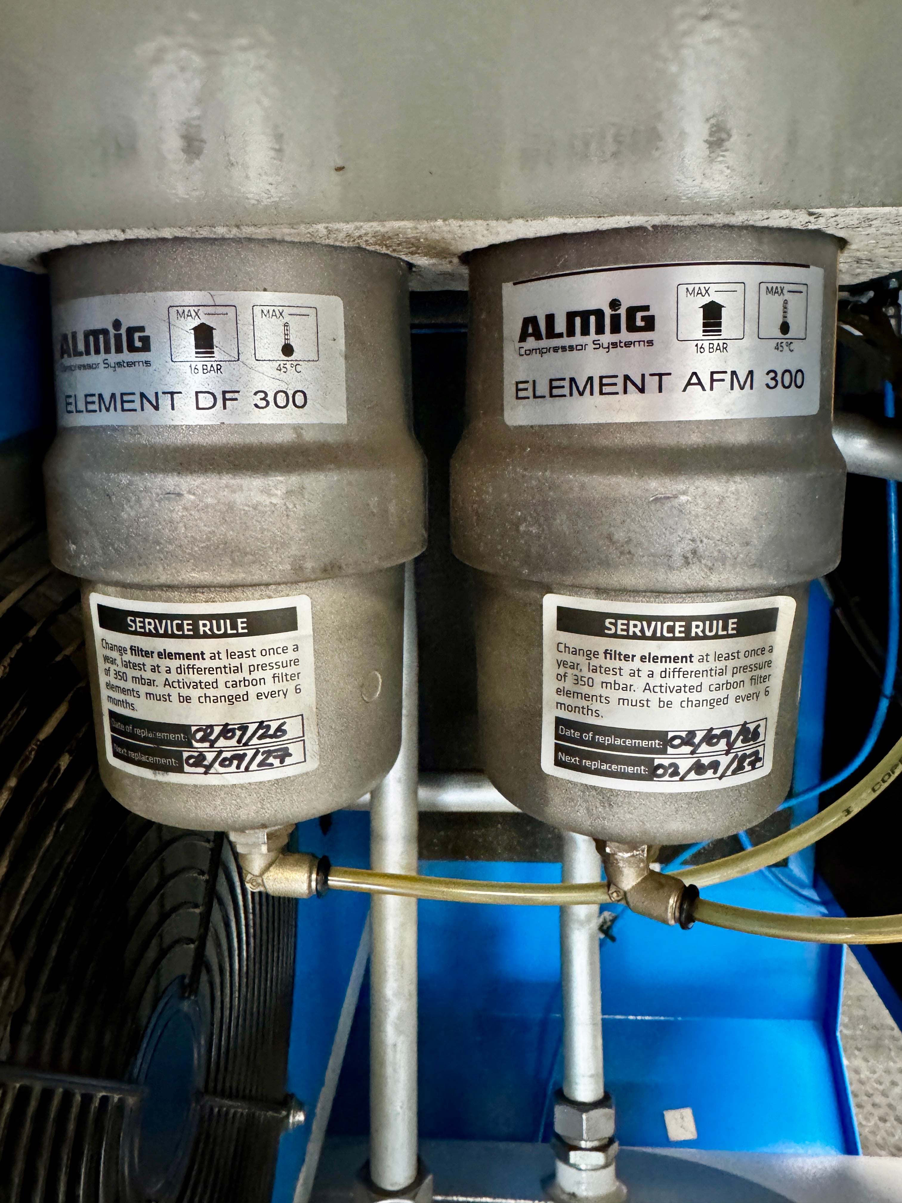 Two Almig compressed air filter elements, labeled Element DF 300 and Element AFM 300, installed side-by-side on a blue machine base.