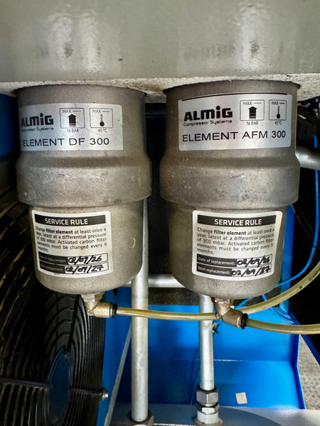 Two Almig compressed air filter elements, labeled Element DF 300 and Element AFM 300, installed side-by-side on a blue machine base.