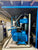 A large blue industrial electric motor and pump assembly housed inside a blue metal cabinet or enclosure, photographed in a workshop or warehouse setting.