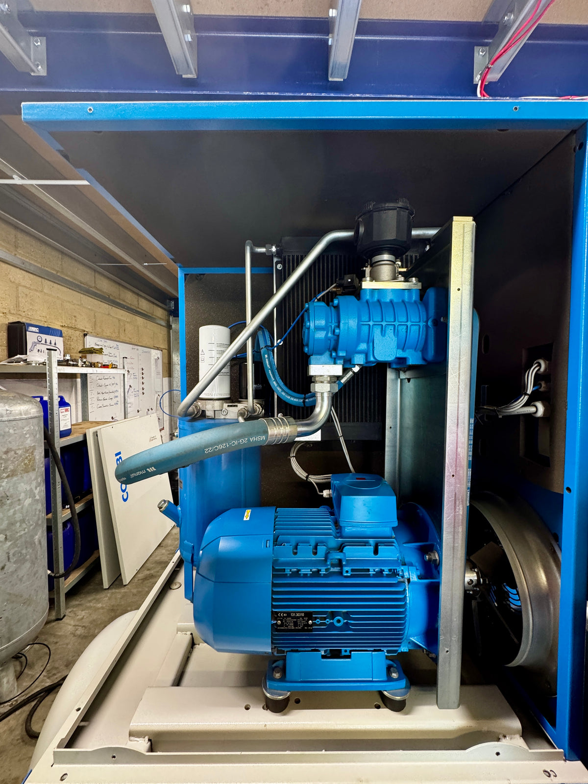 A large blue industrial electric motor and pump assembly housed inside a blue metal cabinet or enclosure, photographed in a workshop or warehouse setting.