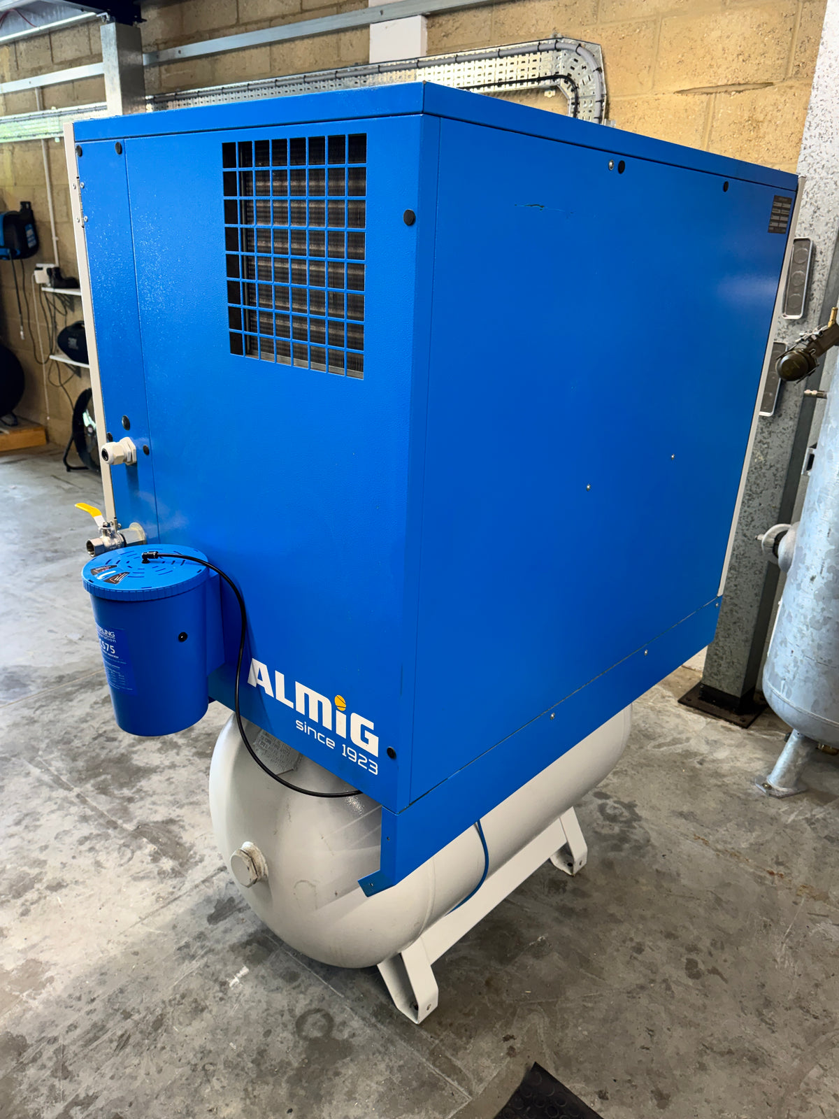 Blue industrial machine with 'Almig' branding on a concrete floor.