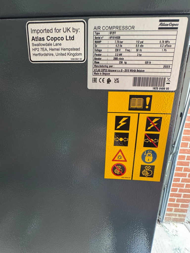 Air compressor with Atlas Copco label and warning stickers on a dark surface.