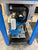 Industrial machine with blue frame and black components on a concrete floor.