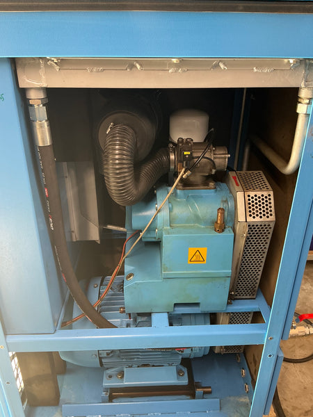 Close-up of a blue industrial machine cabinet showing internal components including a metal vented box, flexible hose, motor, and piping.
