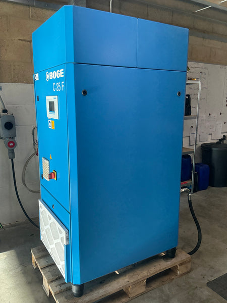 A blue industrial air compressor machine with a digital control panel, mounted on a wooden pallet in an industrial setting.