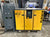 A yellow HPC air compressor unit labeled AS 31 stands on a wooden pallet next to a gray Hertz air receiver tank in a workshop setting.
