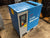 A blue and gray industrial air compressor, specifically a KIMARK MSA F20V 7.5KW unit, photographed in a workshop or warehouse setting on a concrete floor.