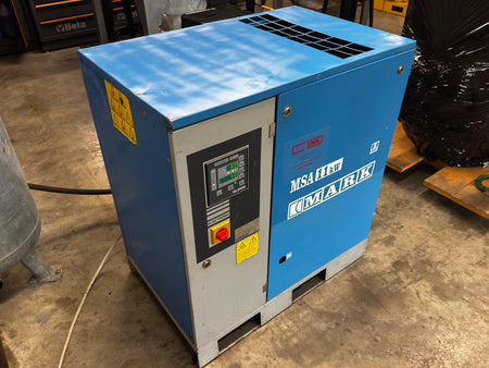 A blue and gray industrial air compressor, specifically a KIMARK MSA F20V 7.5KW unit, photographed in a workshop or warehouse setting on a concrete floor.