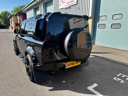 A black SUV parked outdoors in front of a garage building, shown from the rear three-quarter angle. The vehicle has a spare tire mounted on the rear door, black wheels, and a yellow UK license plate reading N700 VAX.