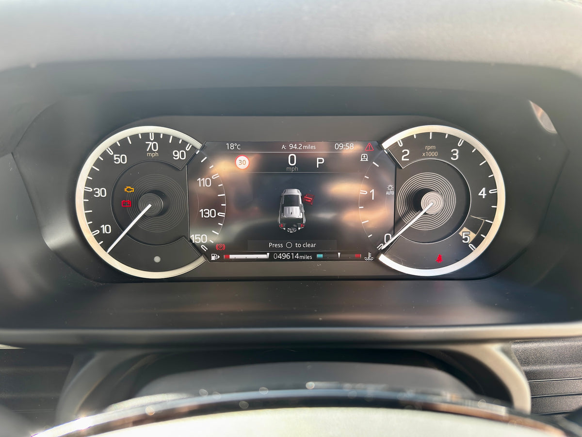 Close-up of a car's digital instrument cluster dashboard display, showing the speedometer, tachometer, and center screen on a dark interior background.