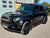A black custom Land Rover Defender SUV parked on an asphalt driveway in front of a garage and brick building.