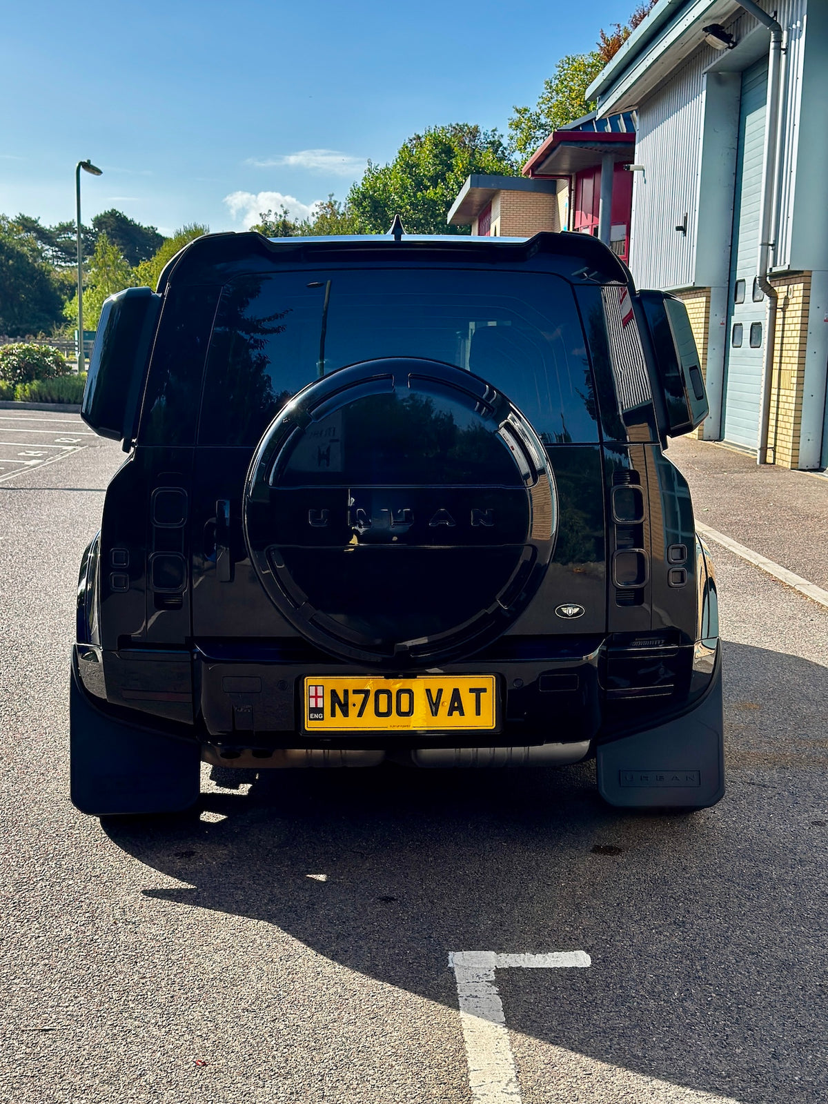 A black Land Rover Defender SUV photographed from the rear, parked on an outdoor paved area with a yellow UK license plate reading N700 VAT.