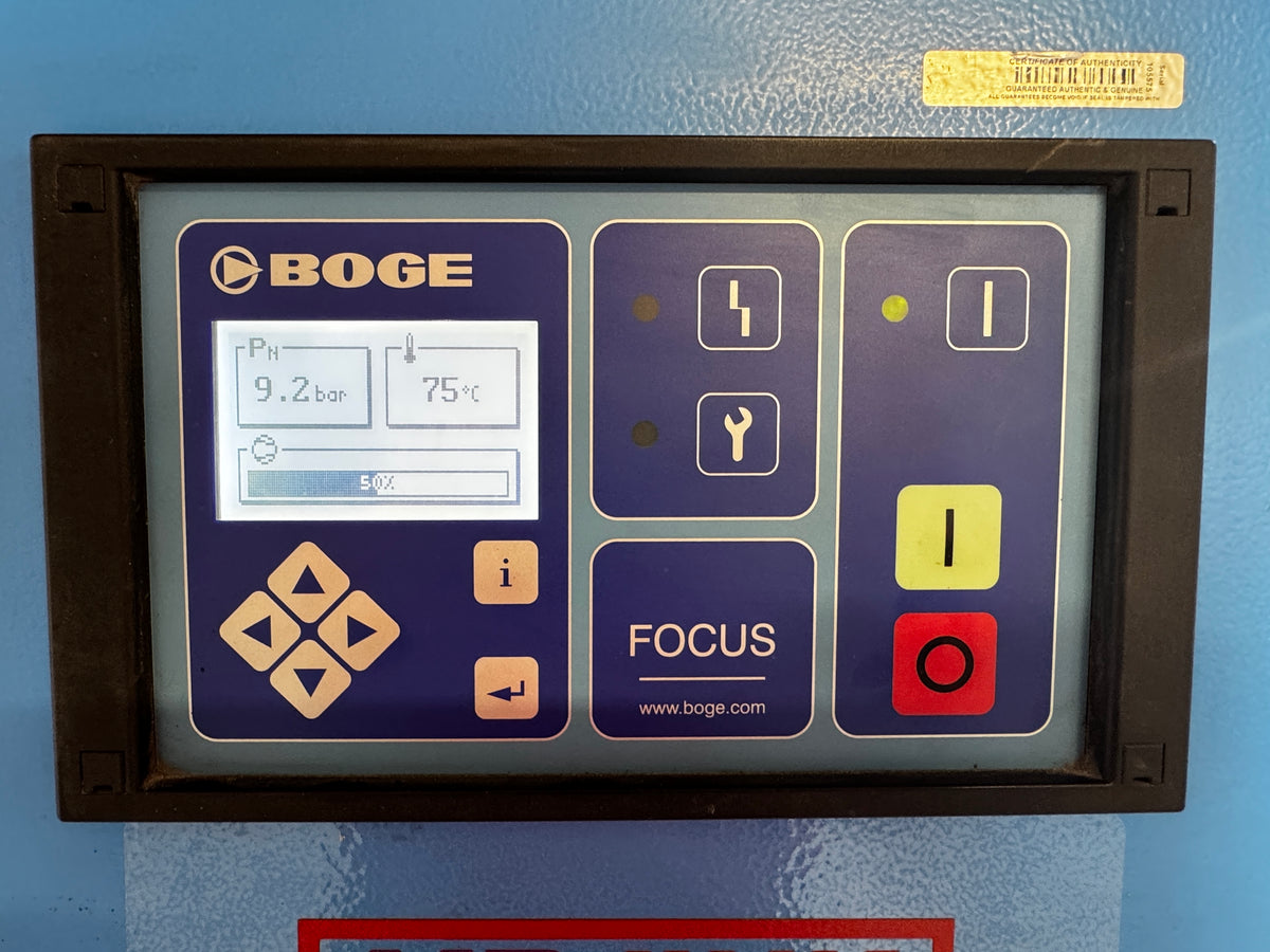 A BOGE industrial touchscreen control panel mounted on a blue metal surface. The panel has a dark frame and a purple faceplate with beige buttons, a white display screen, and red and yellow function buttons.