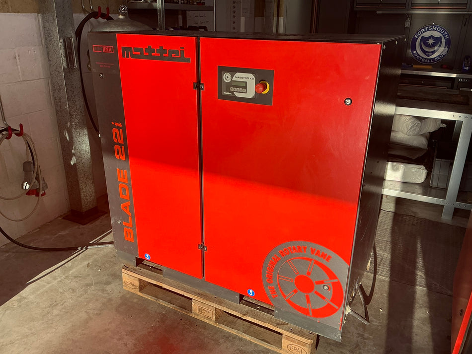 A large red and gray Mattri Blade 22i air compressor sitting on a wooden pallet in an industrial workshop setting.