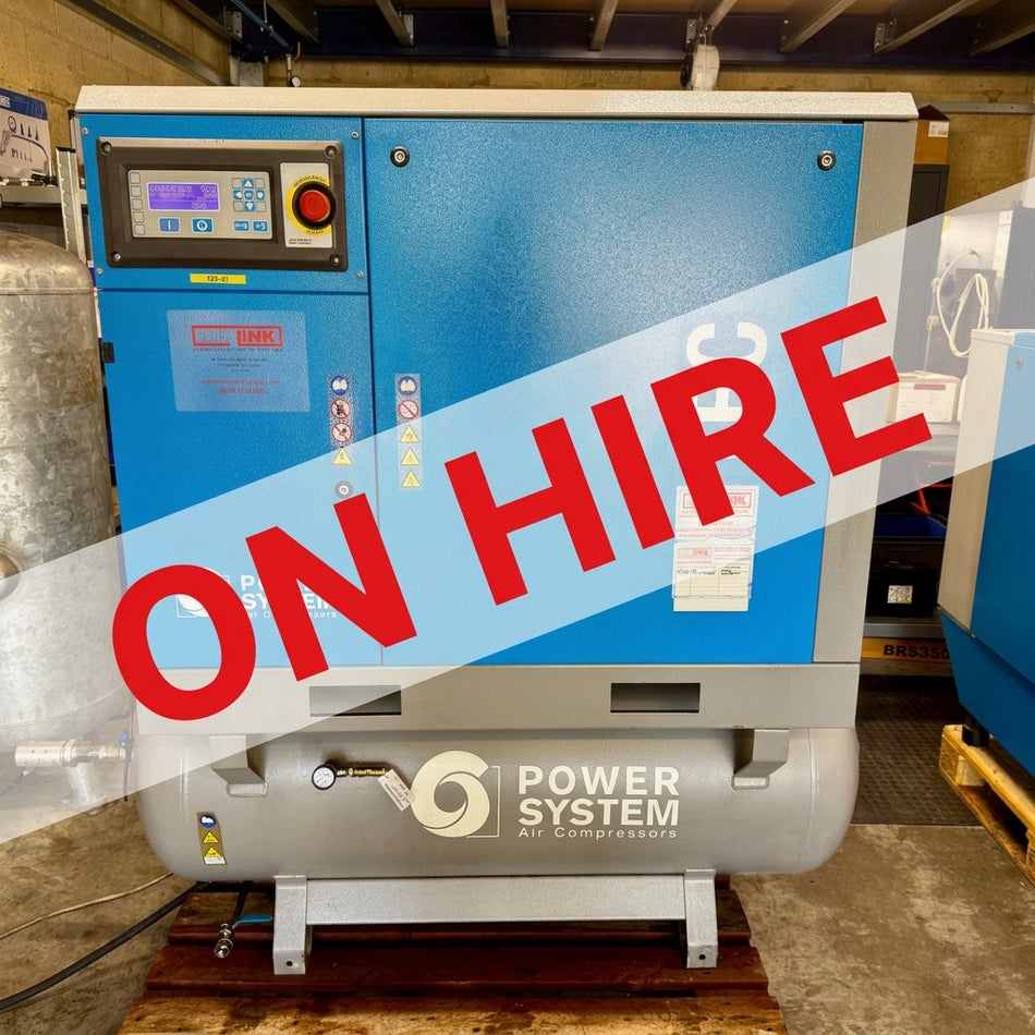 A blue and gray industrial air compressor by Power System TEC, photographed in a workshop or warehouse setting with other machinery visible in the background.