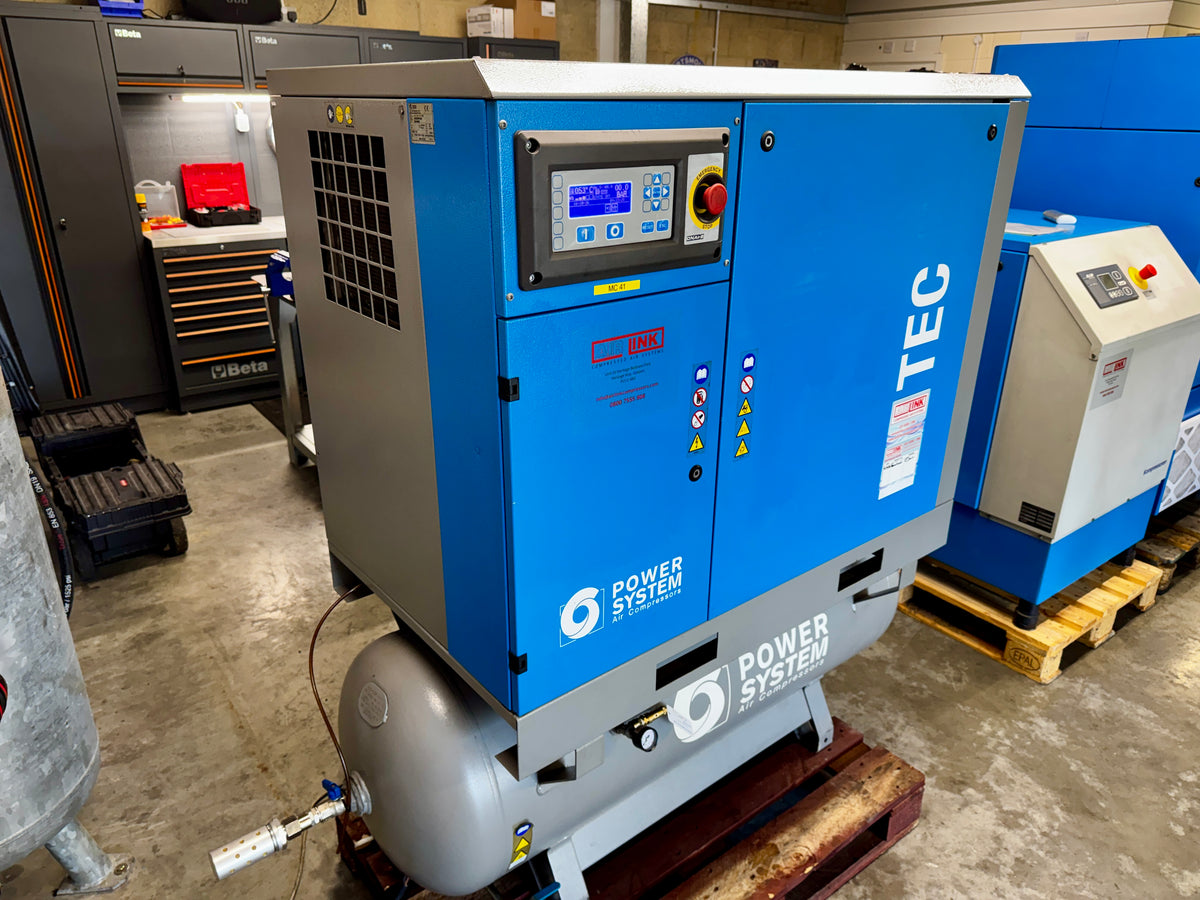A large blue and gray industrial air compressor with a digital control panel and an air receiver tank, photographed in a warehouse or workshop setting.