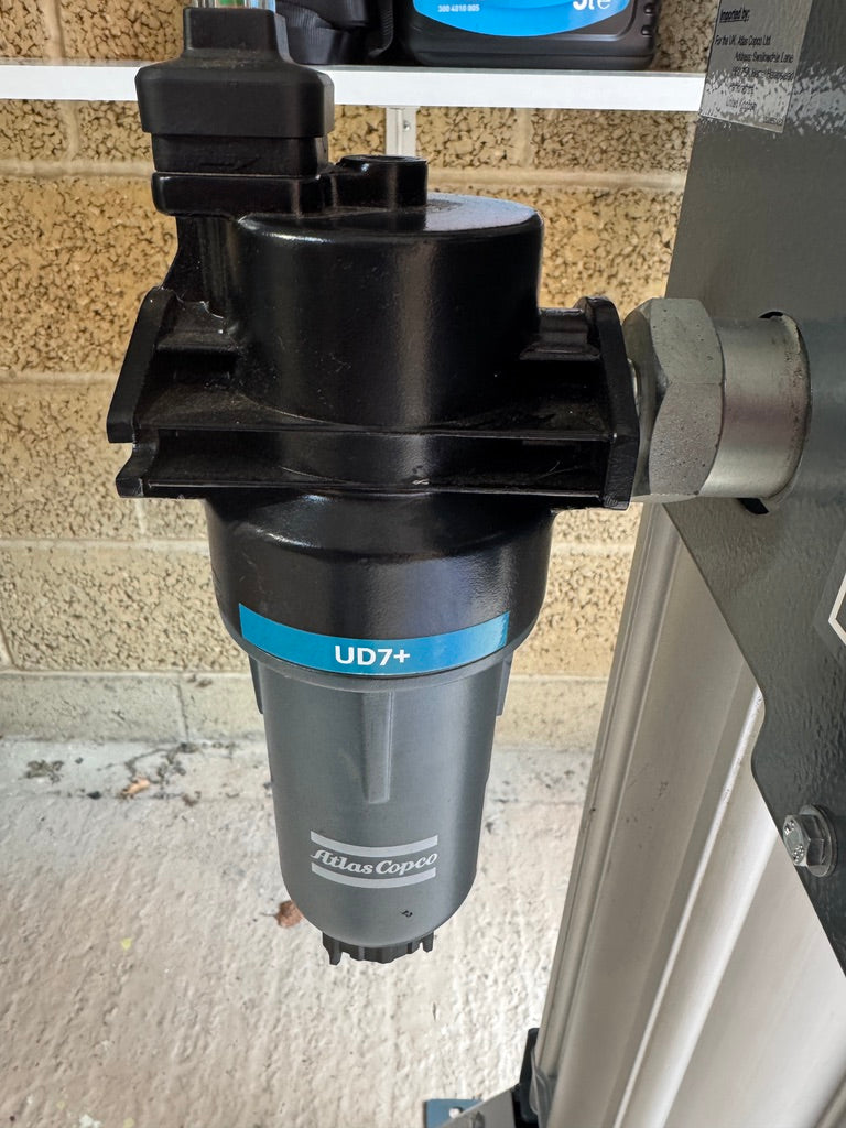 Black filter with 'Atlas Copco' branding on a concrete surface.